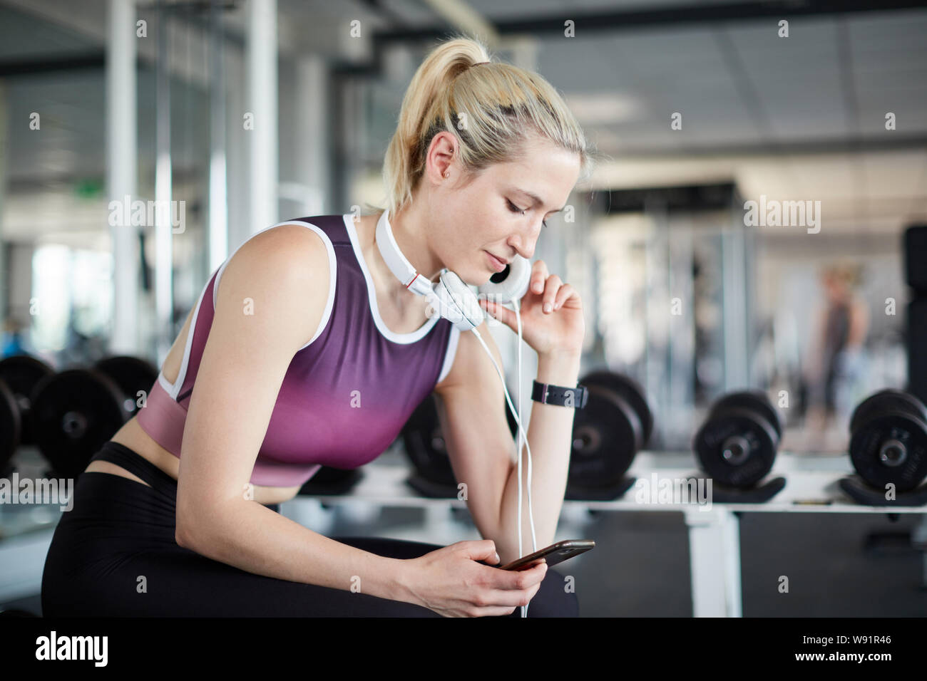 Junge Frau im Fitnesscenter mit Kopfhörern schaut auf Ihrem Smartphone Stockfoto