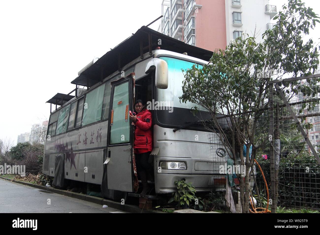 ---- Zhang, Wachmann Sun Jies Frau, sieht in der Tür ihres Hauses, einem umgebauten und solar Bus, Songjiang District, Shanghai, Chi Stockfoto