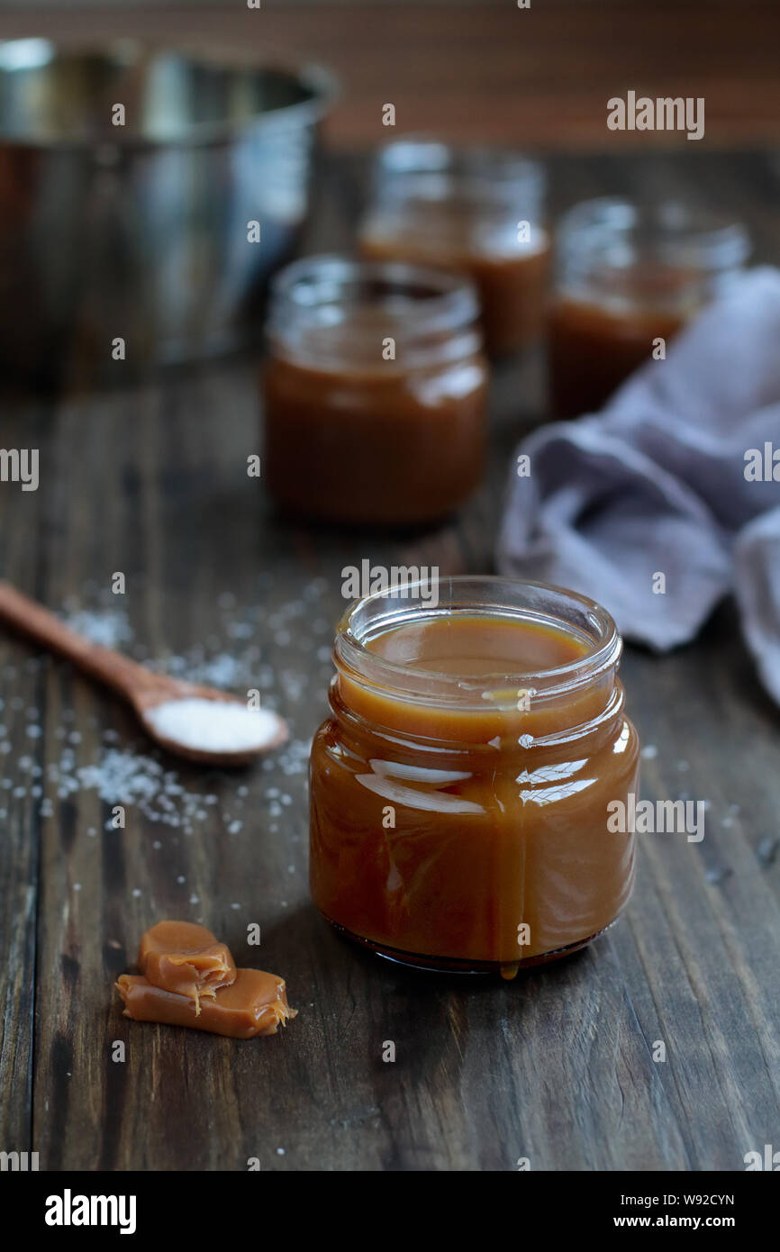 Kleine Gläser gesalzen Karamell Sauce über eine rustikale Tabelle. Selektiver Fokus mit unscharfem Hintergrund. Stockfoto