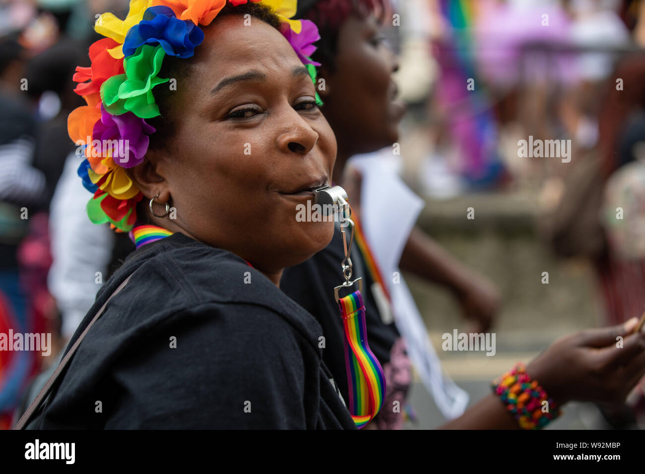 Ein lächelndes Parade goer trägt einen regenbogenfarbenen Kopfschmuck bläst ihre Pfeifen, wie sie in den Brighton Parade im August 2019 teilnehmen Stockfoto