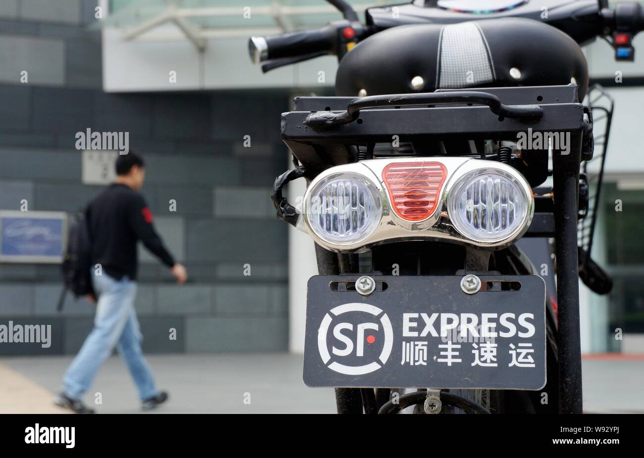 ---- Einen Fußgänger an der Elektrofahrrad einen Kurier von SF Express in Peking, China, 22. April 2012. Chinesische Private Equity Firma Citic Kappe Stockfoto