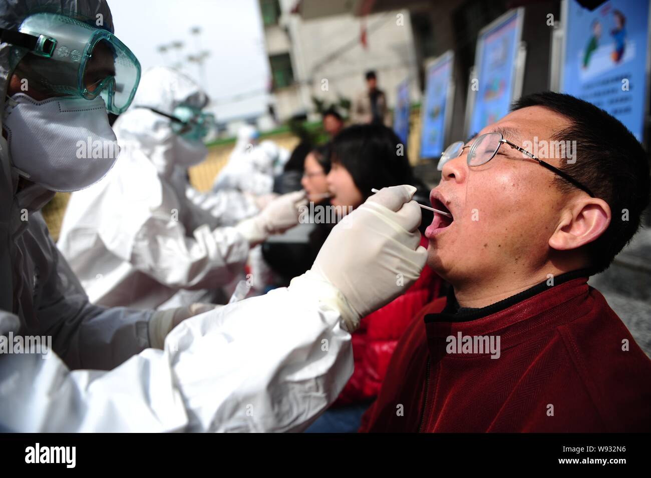 Chinesische Arbeiter aus der lokalen Zentrum für die Prävention und die Kontrolle von Krankheiten, schützende Kleidung, erhält Proben aus dem Mund der particip Stockfoto