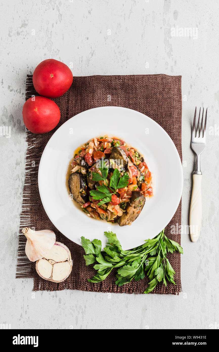Sommer Salat von Auberginen und Tomaten auf einer weißen Platte auf hellem Hintergrund, Ansicht von oben mit Copyspace. Flach. Stockfoto