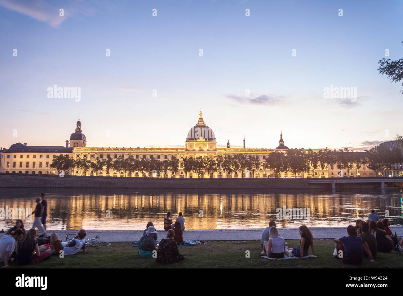 LYON, Frankreich - 18. JULI 2019: Franzosen sitzen am Ufer des Quais de Rhone, gegenüber Hotel Dieu, eines der wichtigsten Denkmäler der Stadt Fo Stockfoto