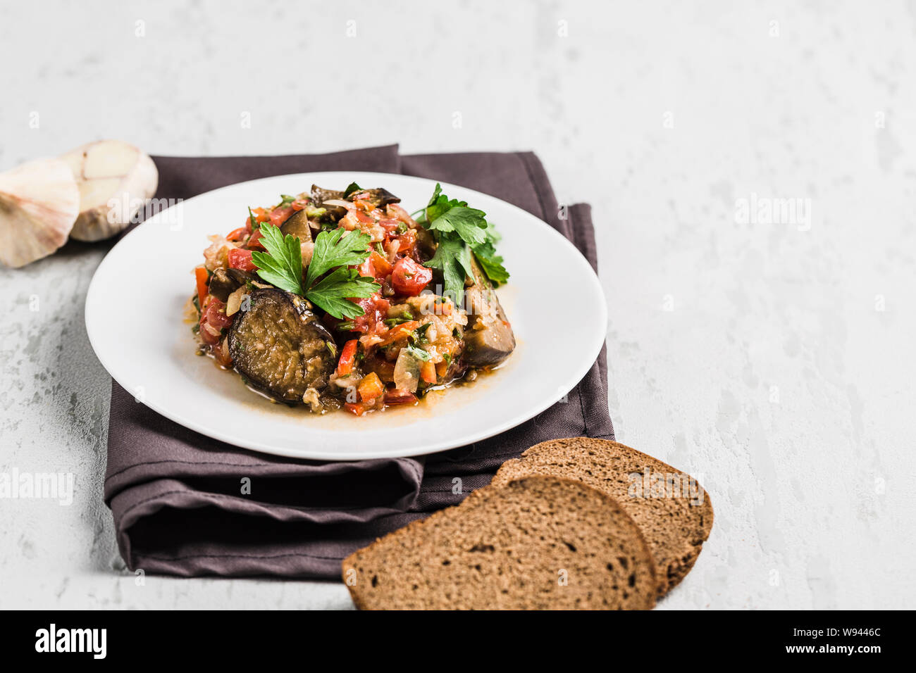 Sommer Salat von Auberginen und Tomaten auf einer weißen Platte auf hellem Hintergrund, Seitenansicht mit Copyspace. Flach. Stockfoto
