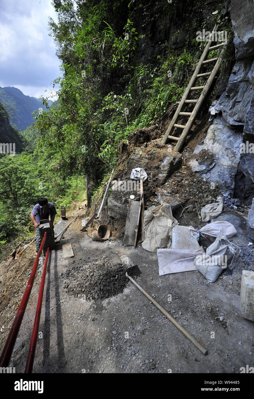 Ein chinesischer Arbeiter konstruiert eine konkrete Schutzgeländer Spalte neben den Himmel Leiter auf der Klippe von einem Berg in Zhangjiawan Dorf, sangzhi County, Zhan Stockfoto