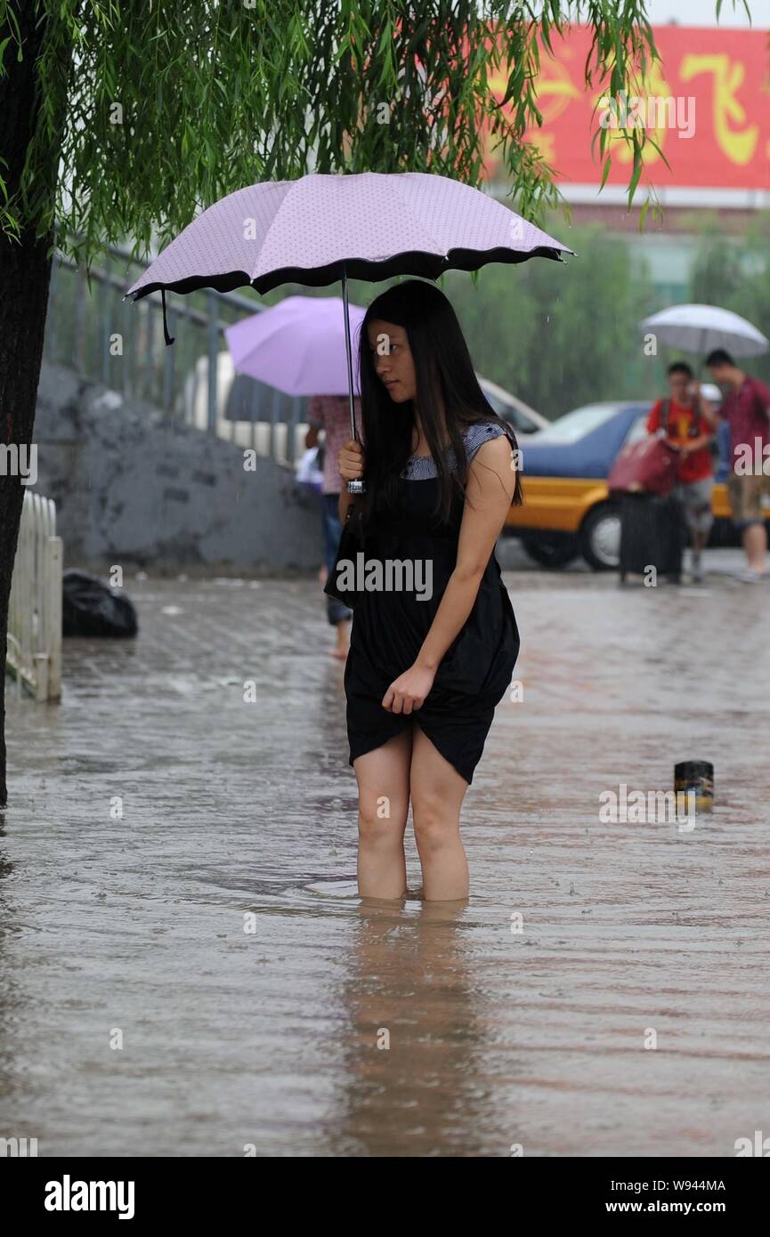 Ein barfüßiger junge Frau hält einen Regenschirm beim Gehen auf eine überschwemmte Straße bei schwerem Regen in Peking, China, 15. Juli 2013. Peking erhöht Safet Stockfoto