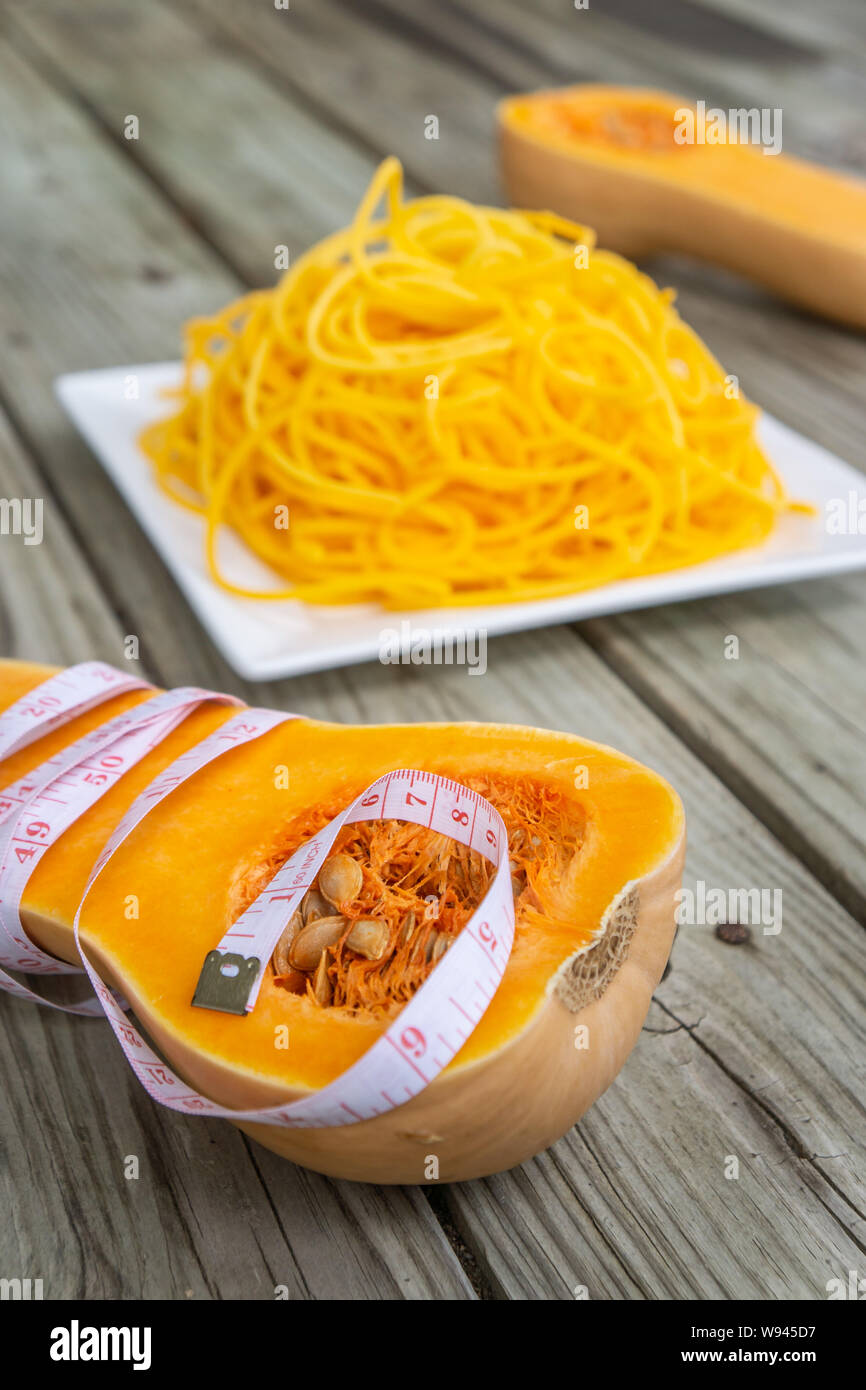 Maßband um butternut Kürbis halbieren mit Low Carb Nudeln im Hintergrund gewickelt. Orange gelb Nudel Pasta - low carb, Getreide, Glu Stockfoto