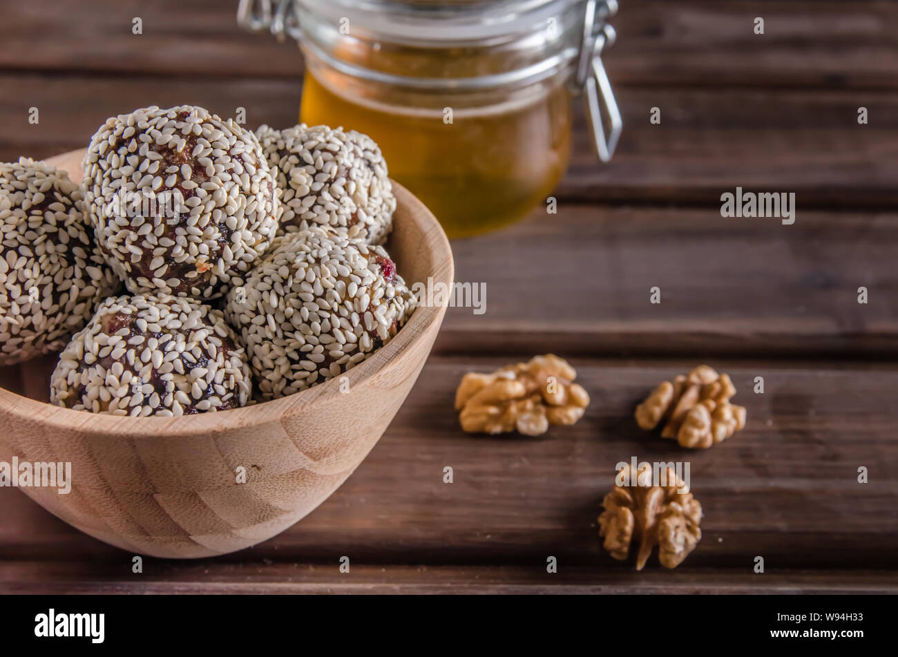 Vegetarische Gerichte, hausgemachte Energie Kugeln von Walnüssen, Datteln, Backpflaumen, Preiselbeeren und Honig mit Sesam auf braunem Holz- Hintergrund Stockfoto