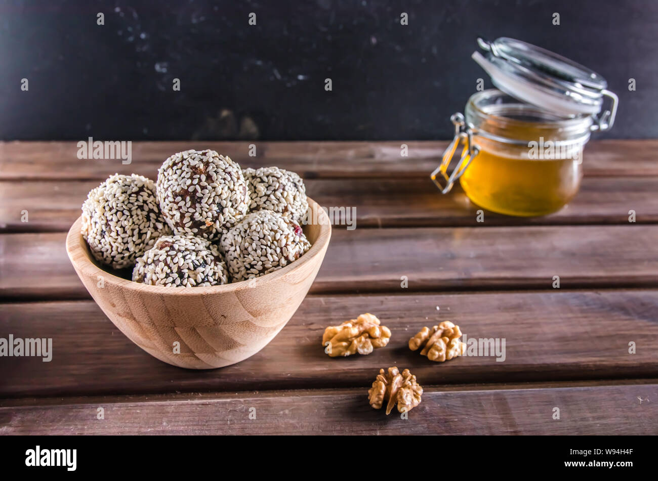 Vegetarische Gerichte, hausgemachte Energie Kugeln von Walnüssen, Datteln, Backpflaumen, Preiselbeeren und Honig mit Sesam auf braunem Holz- Hintergrund Stockfoto