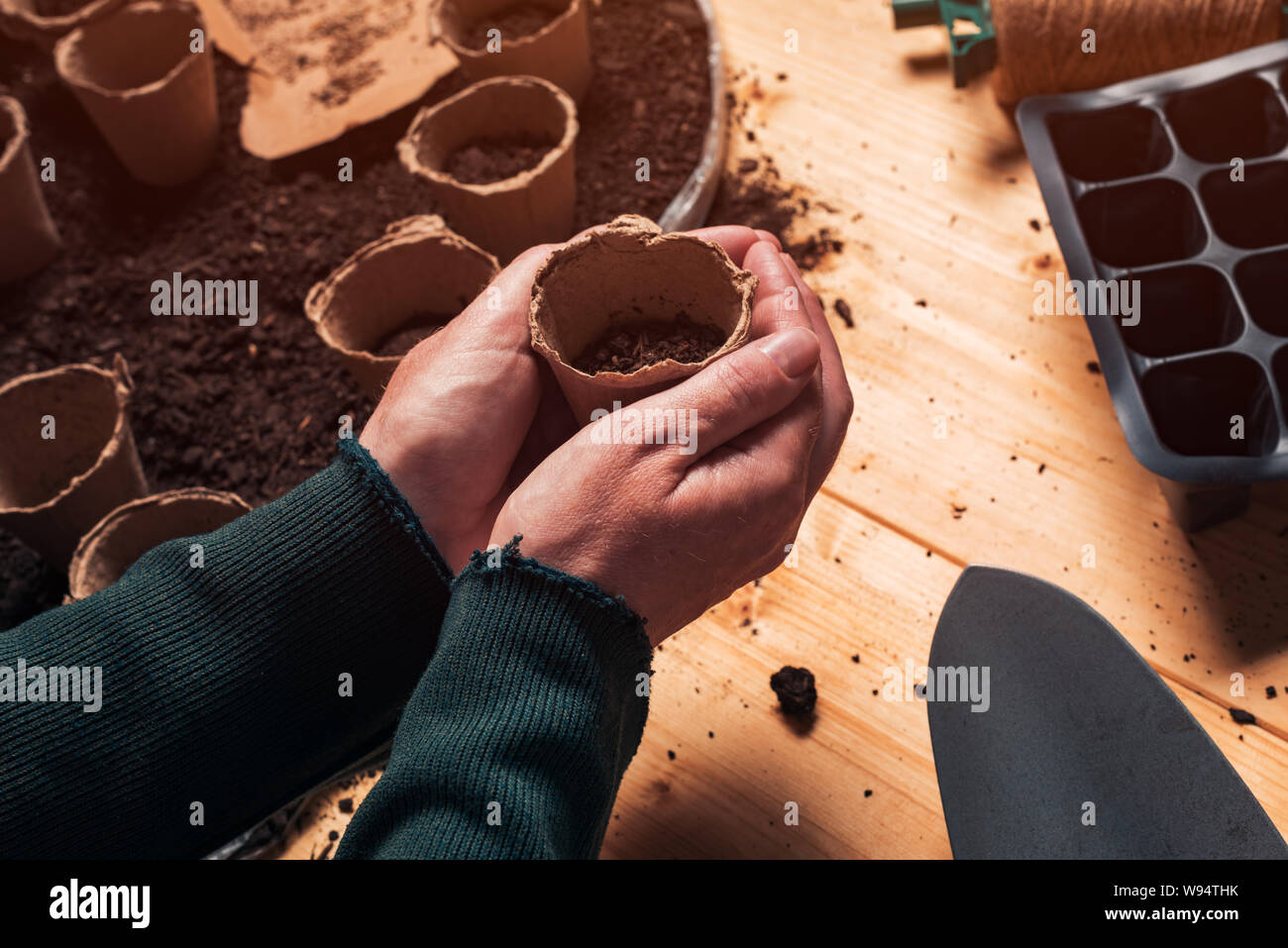 Gärtner mit biologisch abbaubaren Boden pot Container in Händen direkt über der Tabelle, die mit dem ökologischen Landbau und Gartengeräte für homegrown Essen Produ Stockfoto