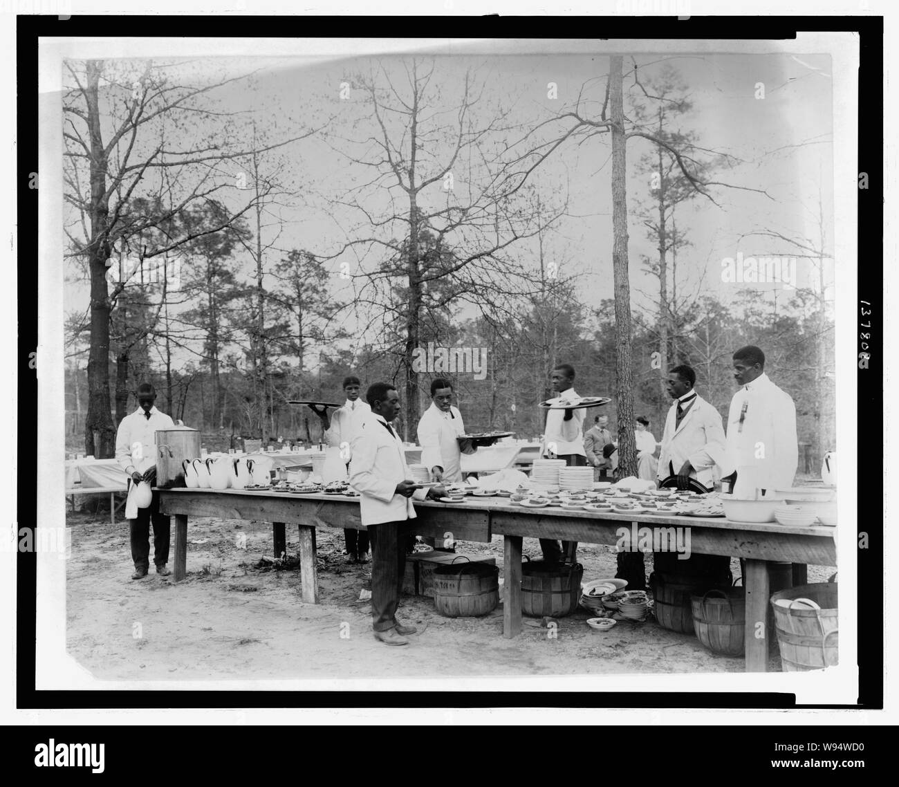 Afroamerikanischen Männern vorbereiten, eine Mahlzeit im Freien unter Bäumen zu dienen Stockfoto