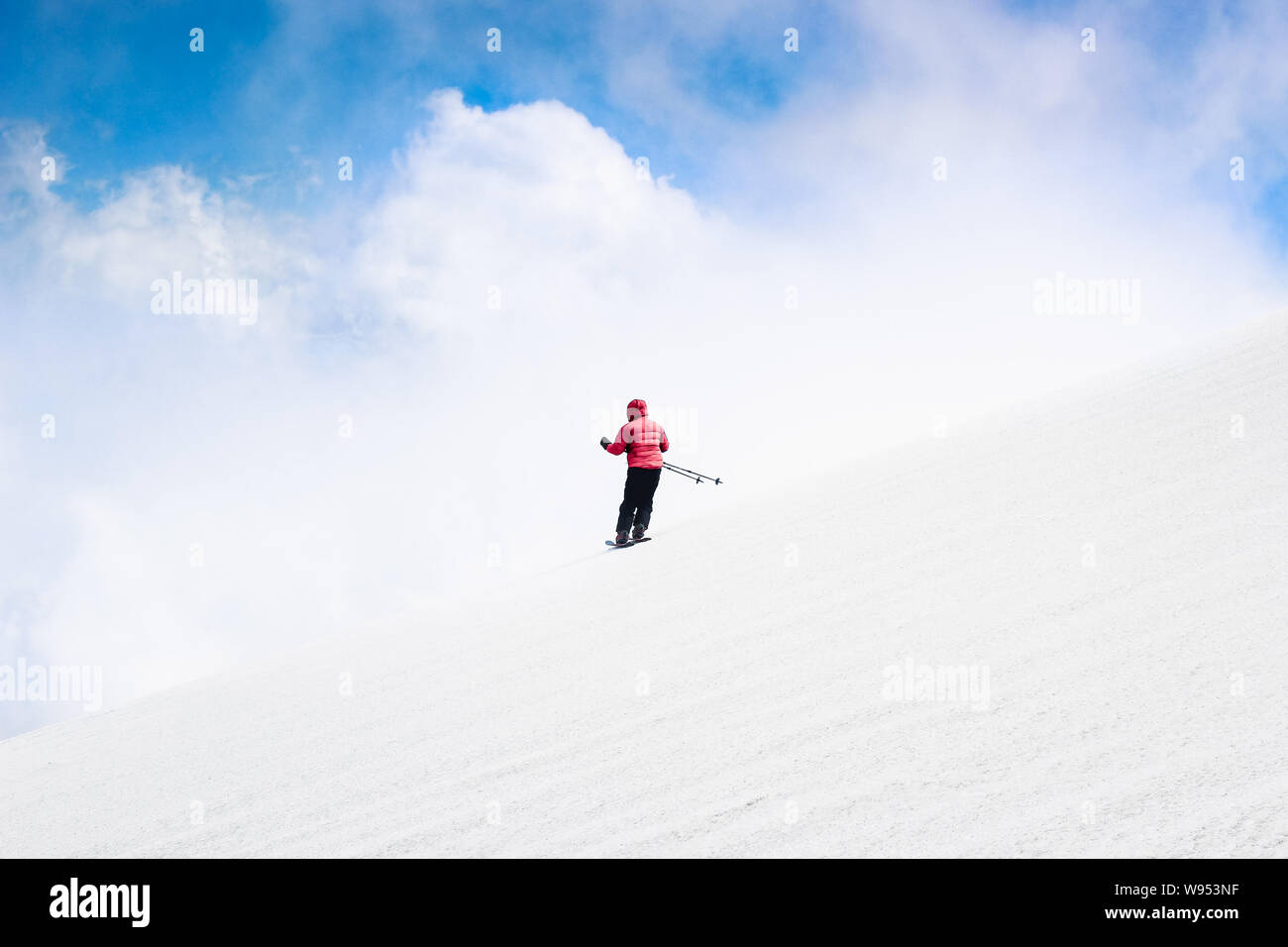 Skier Ski Abfahrt in roter Jacke. Himmel und Wolken hinter dem Horizont. Freeride Ski fahren. Alpine Sports, weißen Schnee. Minimalistische Fotografie. Gefahr, Stockfoto