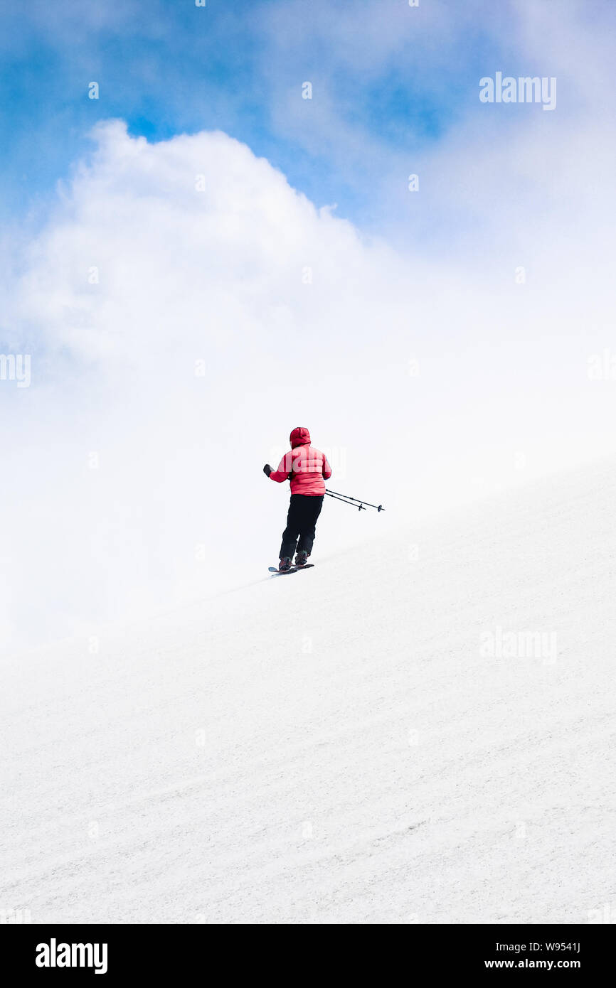 Vertikale Foto von Skifahrer skifahren Abfahrt in roter Jacke. Himmel und Wolken hinter dem Horizont. Freeride Ski fahren. Alpine Sports, weißen Schnee. Minimalistische pho Stockfoto
