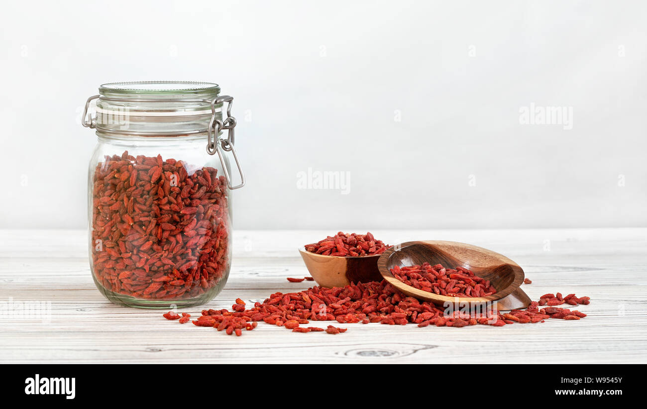 Getrocknete Goji aka. wolfberry in Glas Flasche, einige in hölzernen Schüsseln und auf Whiteboards Schreibtisch verschüttet, Platz für Text, Rechts Stockfoto