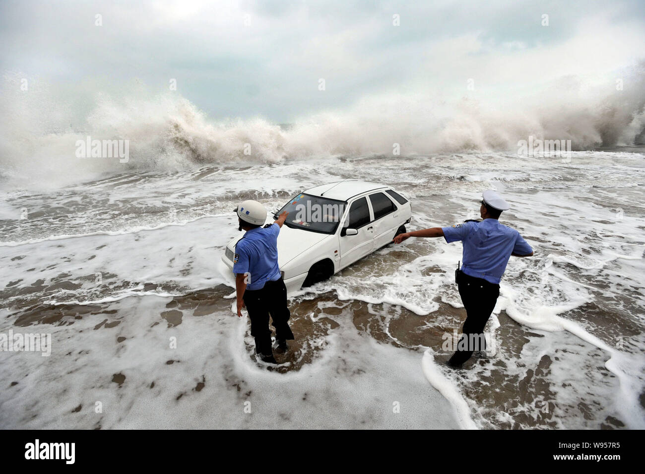 Polizisten direkt ein Auto als riesige Wellen verursacht durch Tyhpoon Bolaven zu verlassen das Meer Wand in Qingdao Stadt schlagen, East China Provinz Shandong, 28 Augu Stockfoto