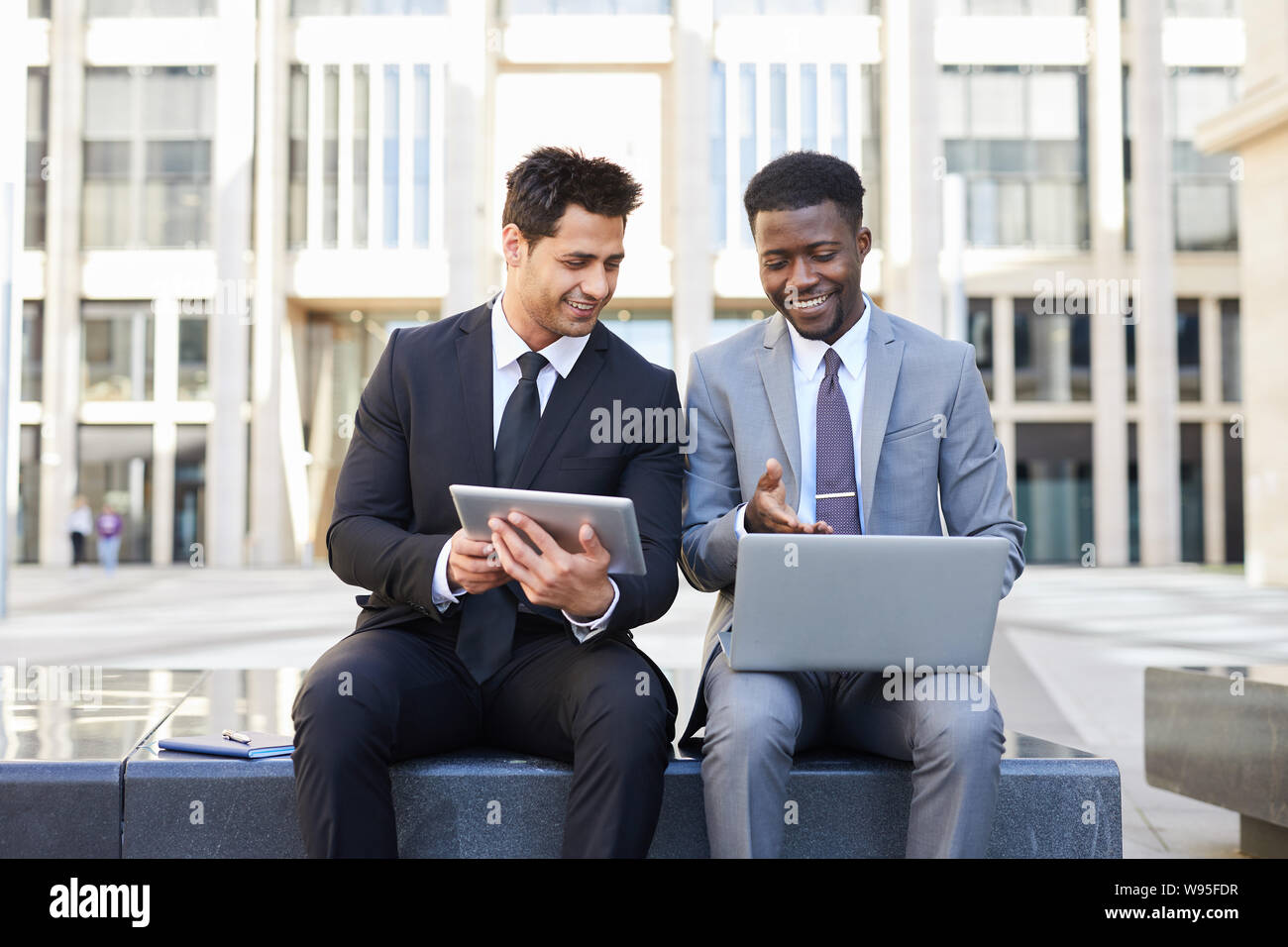 Zwei Geschäftsleute sitzen draußen miteinander reden und arbeiten auf digital Tablet-PC und Laptop. Stockfoto