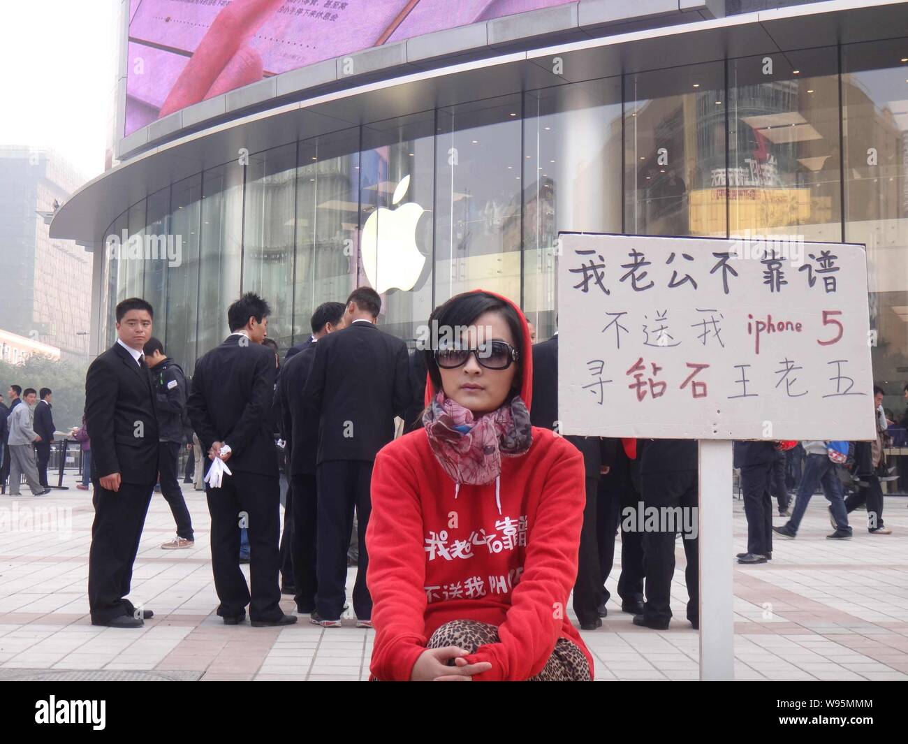 Eine junge chinesische Frau, die neben einem Plakat mit Schildern mit der Aufschrift sitzt, mein Mann nicht zuverlässig ist, er mich nicht ein iPhone kaufen 5, ich bin auf der Suche nach einem reichen m Stockfoto