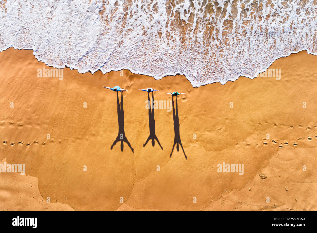 Drei Menschen, die Wellen des Pazifischen Ozeans auf einer sauberen, breiten Sandstrand während der Übung in der Luft von oben nach unten anzeigen. Stockfoto