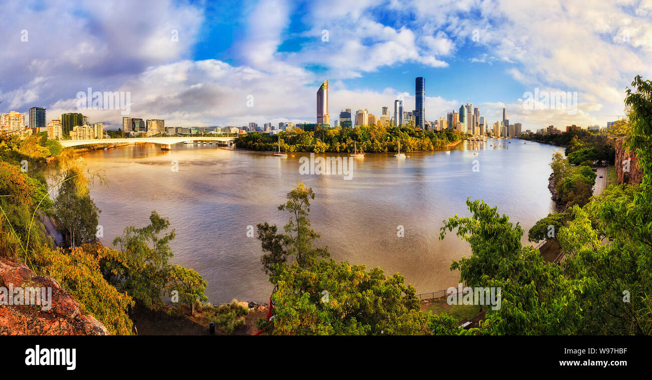 Grüne frische Klippen Park am Ufer des Brisbane River über Stadt CBD hoch aufragenden Türmen in weiten Panorama auf sonnigen Morgen unter blauem Himmel. Stockfoto