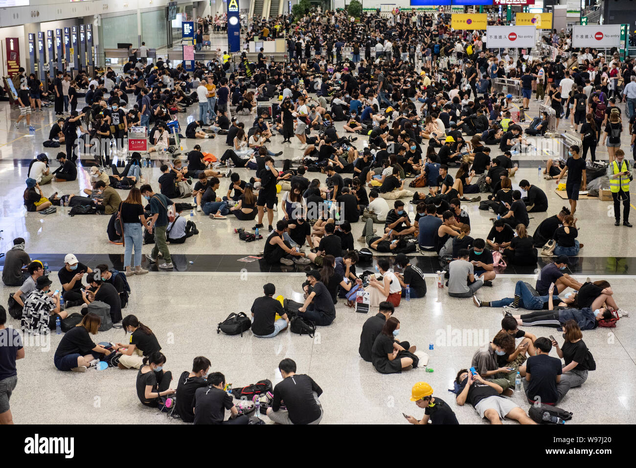 Passagiere und regierungsfeindlichen Demonstranten an der Hong Kong International Airport bei einem Sit-in Demonstration versammeln. In Antwort vom Wochenende Gewalt, die eine Frau in die Augen, mit einem Projektil während der Auseinandersetzungen zwischen Demonstranten und der Polizei erschossen wurde, regierungsfeindlichen Demonstranten besetzten Hong Kong International Airport und zwang die Annullierung von Flügen. Stockfoto
