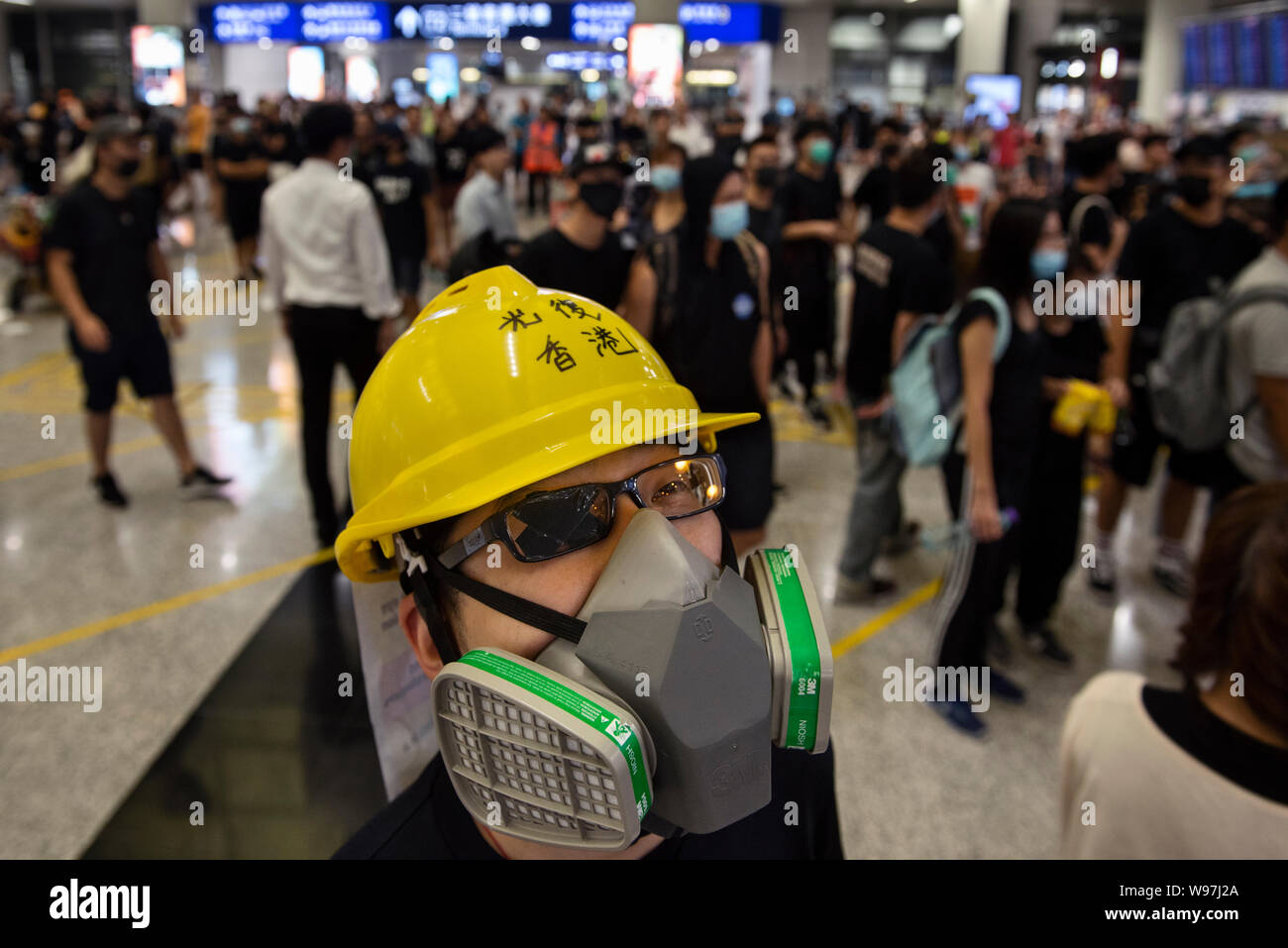 Eine Demonstrantin trägt einen Helm, Gas Mask und Augenklappe bei einem Sit-in Protest am internationalen Flughafen Hong Kong entfernt. In der Antwort aus dem Wochenende Gewalt, die eine Frau in die Augen, mit einem Projektil während der Auseinandersetzungen zwischen Demonstranten und der Polizei erschossen wurde, regierungsfeindlichen Demonstranten besetzten Hong Kong International Airport und zwang die Annullierung von Flügen. Stockfoto