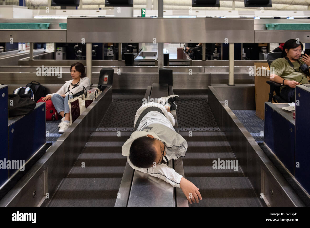 Eine gestrandete Passagiere schläft am Check-in-Schalter Riemen an der Hong Kong International Airport während des Protestes. In Antwort vom Wochenende Gewalt, die eine Frau in die Augen, mit einem Projektil während der Auseinandersetzungen zwischen Demonstranten und der Polizei erschossen wurde, regierungsfeindlichen Demonstranten besetzten Hong Kong International Airport und zwang die Annullierung von Flügen. Stockfoto