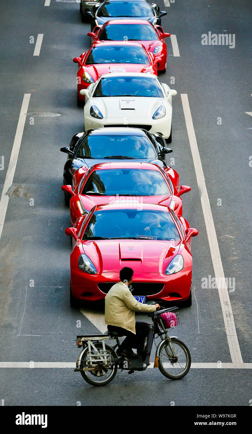 Ein Radfahrer fährt hinter Ferrari Sportwagen in der Linie auf der Straße während einer Parade anlässlich des 20-jährigen Jubiläums des Ferraris Präsenz in China zu feiern, in Guang Stockfoto