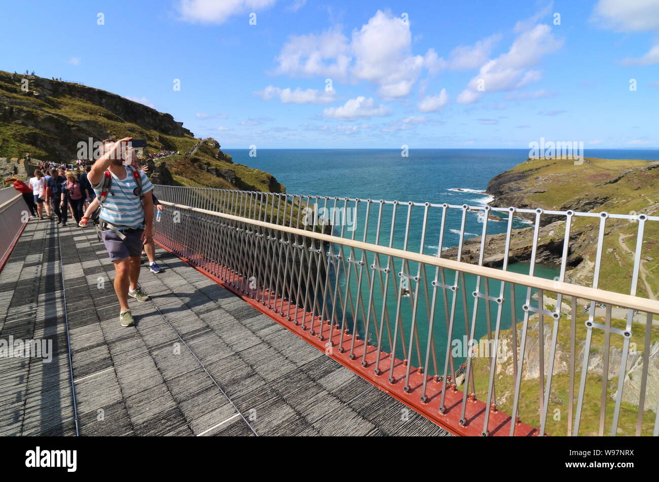 Menschen auf die umstrittene neue Fußgängerbrücke re-Verbindung beider Hälften des Tintagel Castle zum ersten Mal in 500 Jahren, hat endlich geöffnet. Die mittelalterliche Burg an der Küste von Cornwall - lange gemunkelt, die Website von König Arthur's legendären Camelot zu sein - die ursprüngliche Brücke verloren irgendwann zwischen dem 15. und 16. Jahrhundert. Ein Sturm, der die kornischen Küste treffen verzögerte Eröffnung der Brücke. Stockfoto