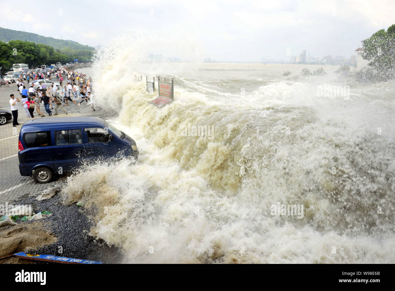 Besucher und Anwohner wie Wellen aus einem Tidal Bore Schwankung hinter eine Absperrung und ein Fahrzeug am Ufer des Qiantang Fluss in Hangzhou City, East C Stockfoto