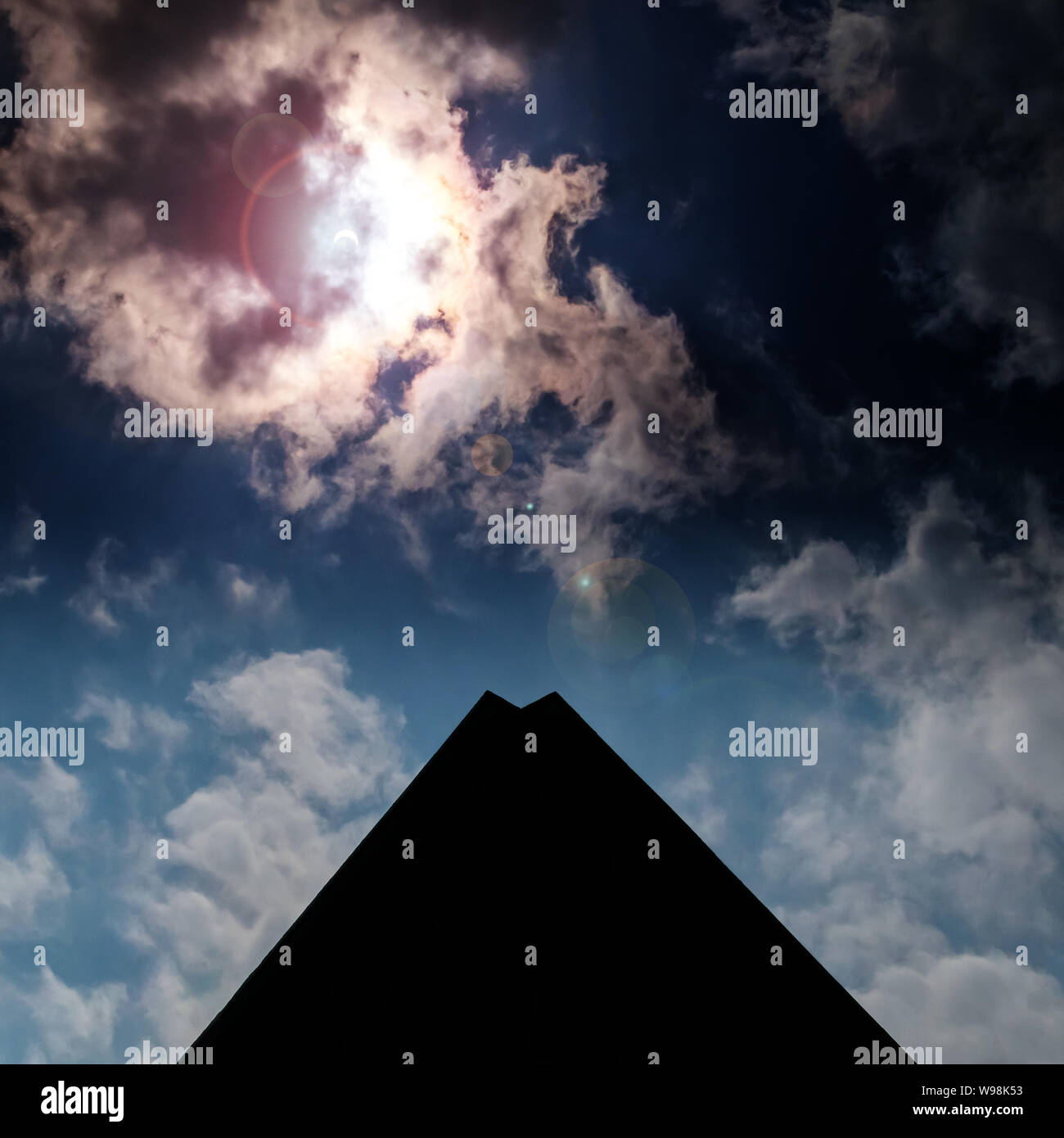 Sonnenfinsternis scheint durch die Wolken am Himmel über einem schwarzen pyramidenförmigen Gebäude Stockfoto