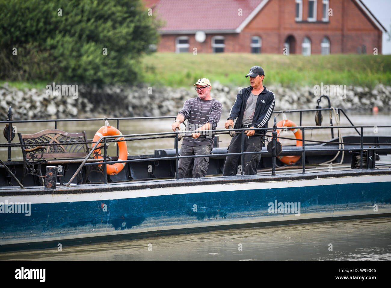 Leer, Deutschland. 11. Juli, 2019. Arnold Höge (l) und Oliver Grensemann, sowohl ferrymen, ziehen Sie die Fähre "pünte" mit Ihren Händen auf dem Fluß "jümme". Dank der Kraft der Gezeiten und starke Muskeln, eine kleine Fähre den Fluss Jümme Kreuze in Ostfriesland. Credit: mohssen Assanimoghaddam/dpa/Alamy leben Nachrichten Stockfoto