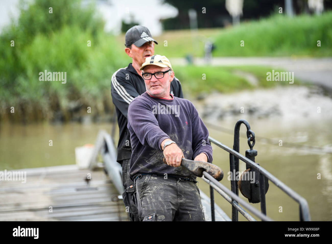 Leer, Deutschland. 11. Juli, 2019. Die ferrymen Arnold Höge (vorne) und Oliver Grensemann ziehen die Fähre Pünte mit ihren Händen über den Fluss Jümme. Dank der Kraft der Gezeiten und starke Muskeln, eine kleine Fähre den Fluss Jümme Kreuze in Ostfriesland. Credit: mohssen Assanimoghaddam/dpa/Alamy leben Nachrichten Stockfoto