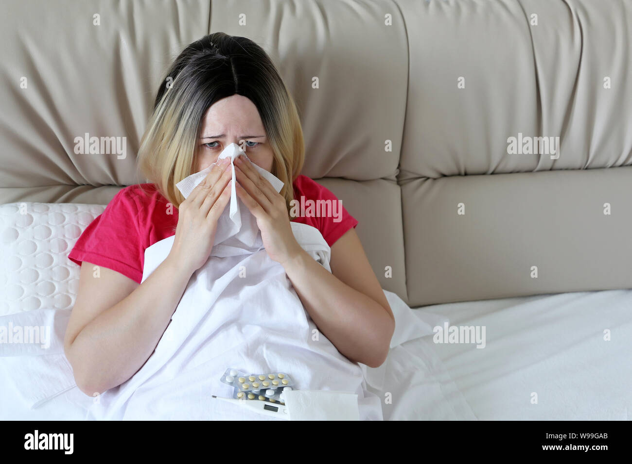 Frau, die ihre Nase weht in ein Taschentuch in einem Bett sitzen. Unglückliche Mädchen leiden, laufende Nase, Konzept der Kranken zu Hause, Erkältungen und Grippe, Fieber Stockfoto