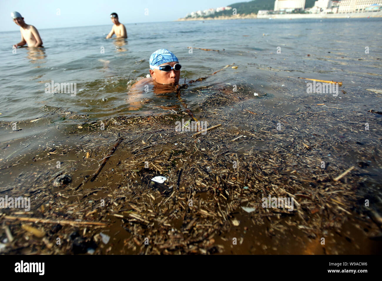Ein chinesischer Mann schwimmt neben dem Müll schwimmend auf dem Wasser an einem Beach Resort in Weihai City, East China Provinz Shandong, 15. September 2010. Th Stockfoto