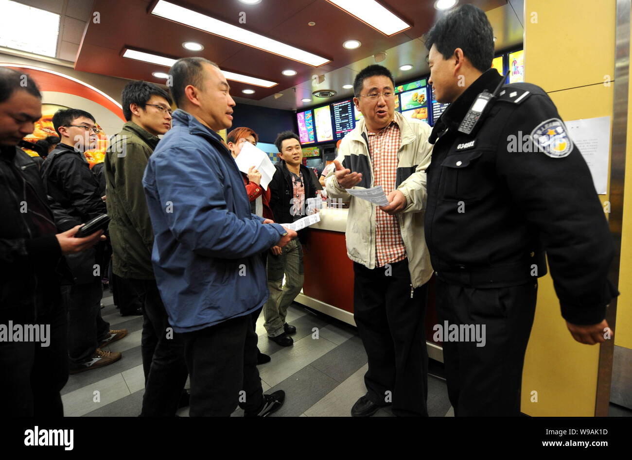 Wütend chinesische Kunden, die Kopien von KFCs online Coupons beschweren sich mit einem Polizisten über KFCs Denial-of-diese Gutscheine an einem KFC Restaurant in Beijin Stockfoto