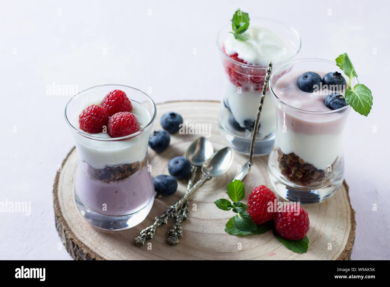 Drei Gläser von leckeren Joghurt und Obst parfaits. Gesund im Frühling und Sommer Snack serviert mit Minze auf Holzbrett Stockfoto