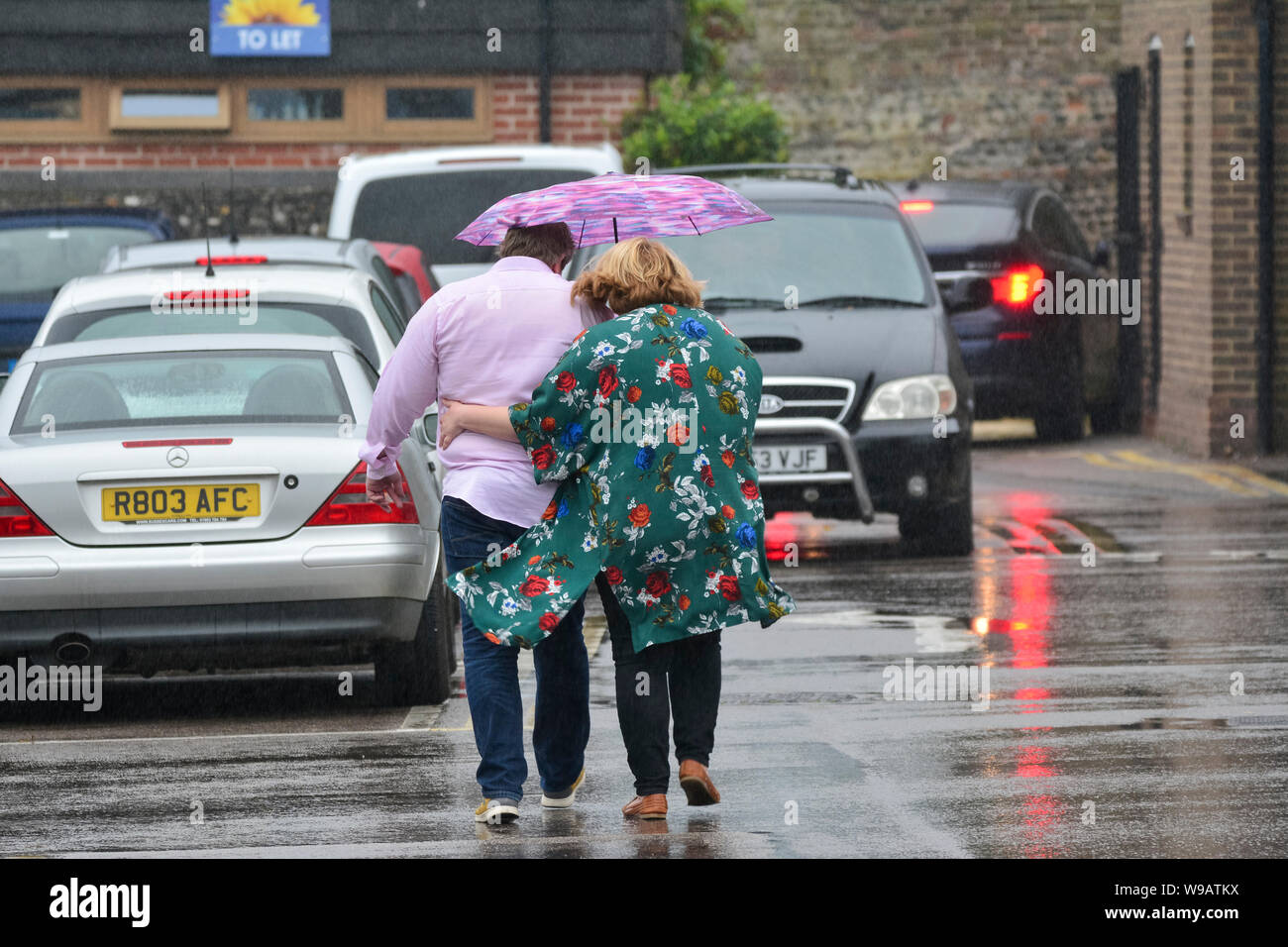 Ein paar Leute heraus in den regen Austausch einen Schirm verfangen, Position für ein Auto in einem Parkhaus an einem regnerischen Tag in Großbritannien. Regen in Großbritannien. Stockfoto