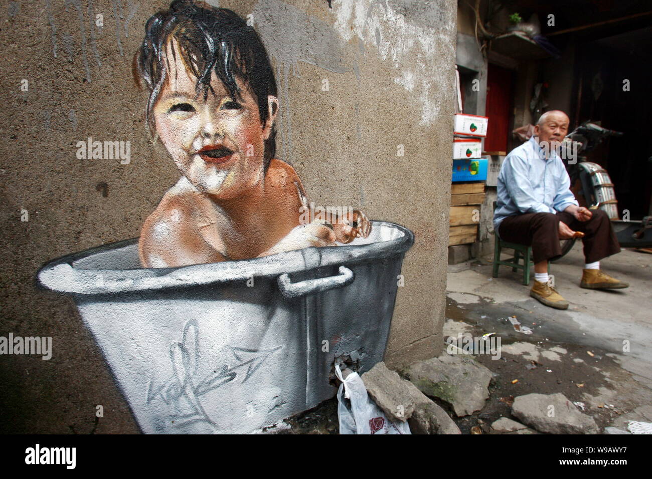 Ein älterer Chinese liegt neben einem Gemälde von einem Kind die Badewanne an die Wand eines Hauses in der Spur eines Slums in Shanghai, China, 26. Mai 2010. Stockfoto