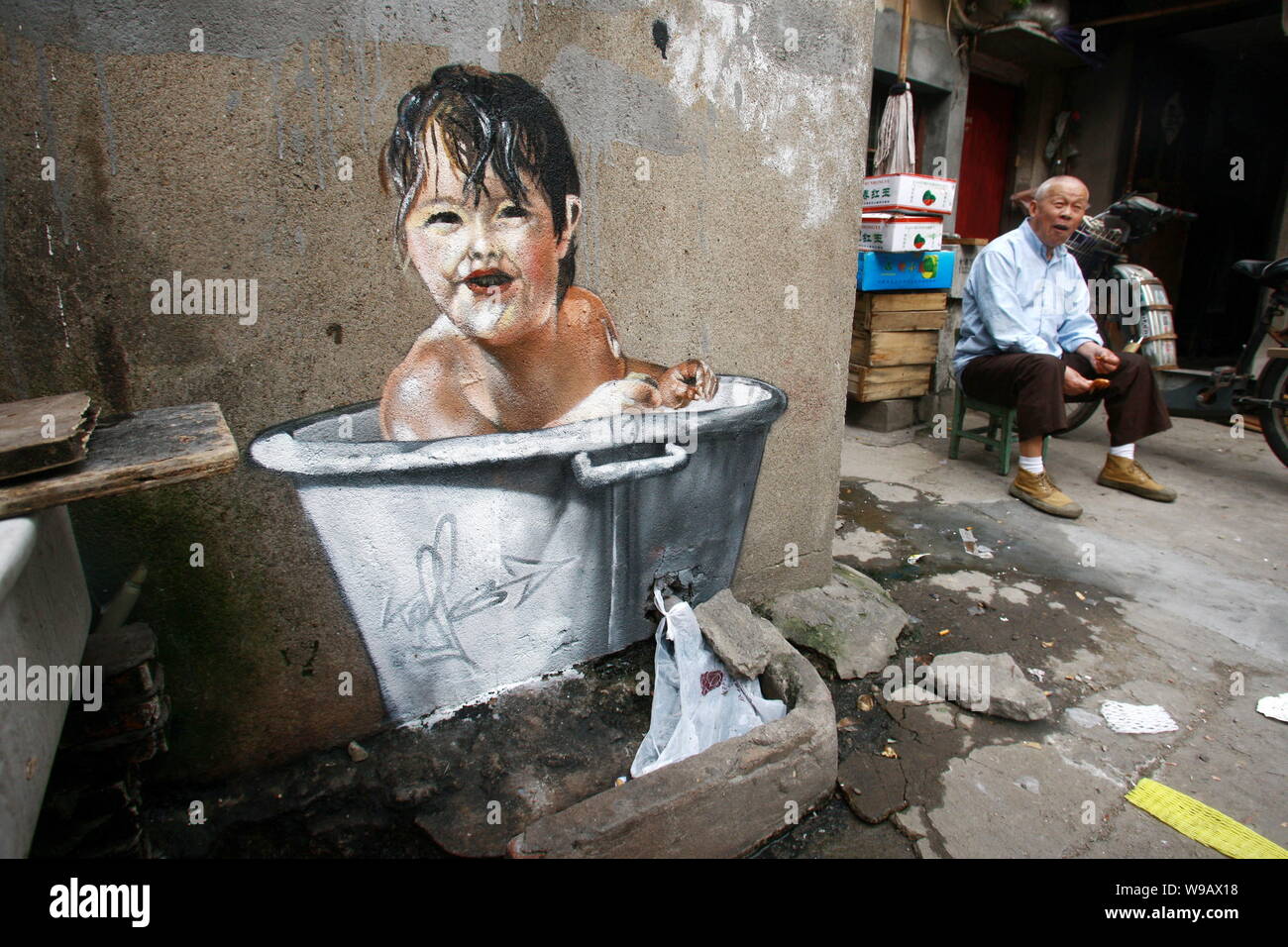 Ein älterer Chinese liegt neben einem Gemälde von einem Kind die Badewanne an die Wand eines Hauses in der Spur eines Slums in Shanghai, China, 26. Mai 2010. Stockfoto