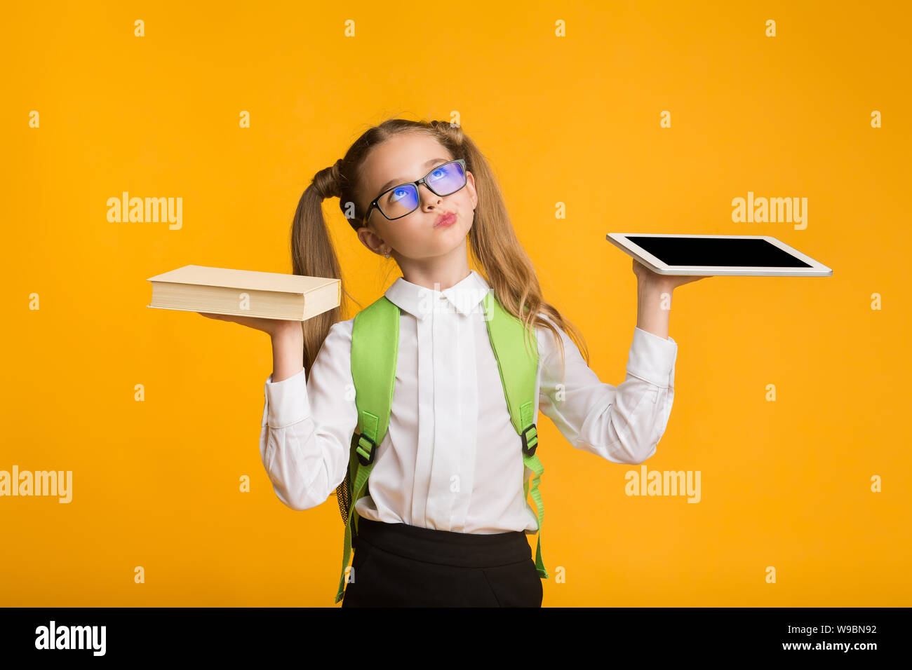 Kleines Schulmädchen Vergleich Buch und Tablet auf gelbem Hintergrund Stockfoto