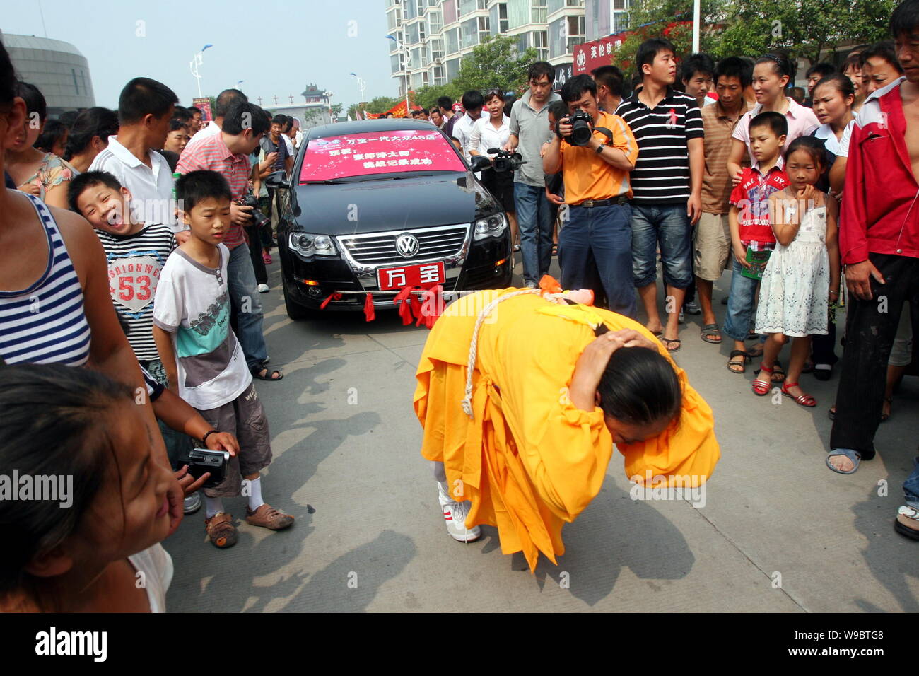 Die chinesischen Leute schauen auf buddhistische Nonne Zhang Tingting ziehen 8 Autos mit ihren Haaren während der letzten Leistung vor der Rasur Ihr Haar zu werden, eine von Stockfoto