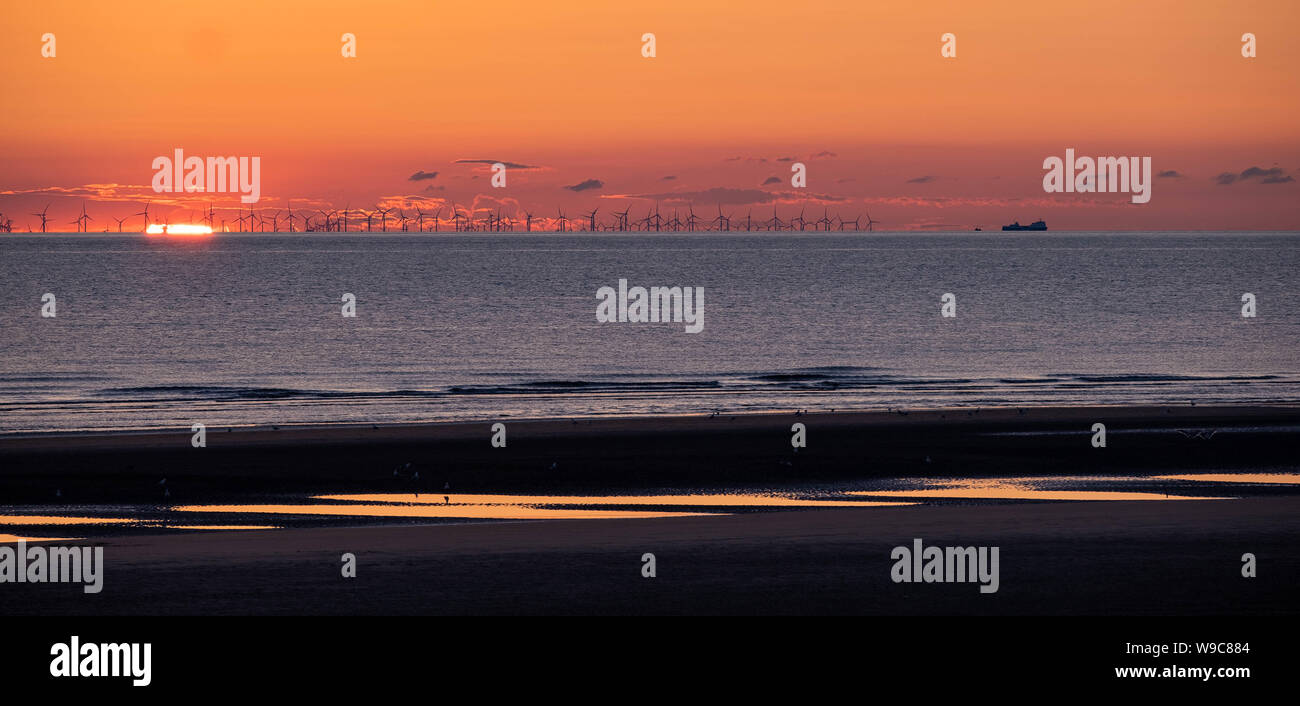 Ein ruhiger Sonnenuntergang über der Irischen See, von einem Strand mit Mustern im Sand und einem Windpark am Horizont mit der untergehenden Sonne. Stockfoto
