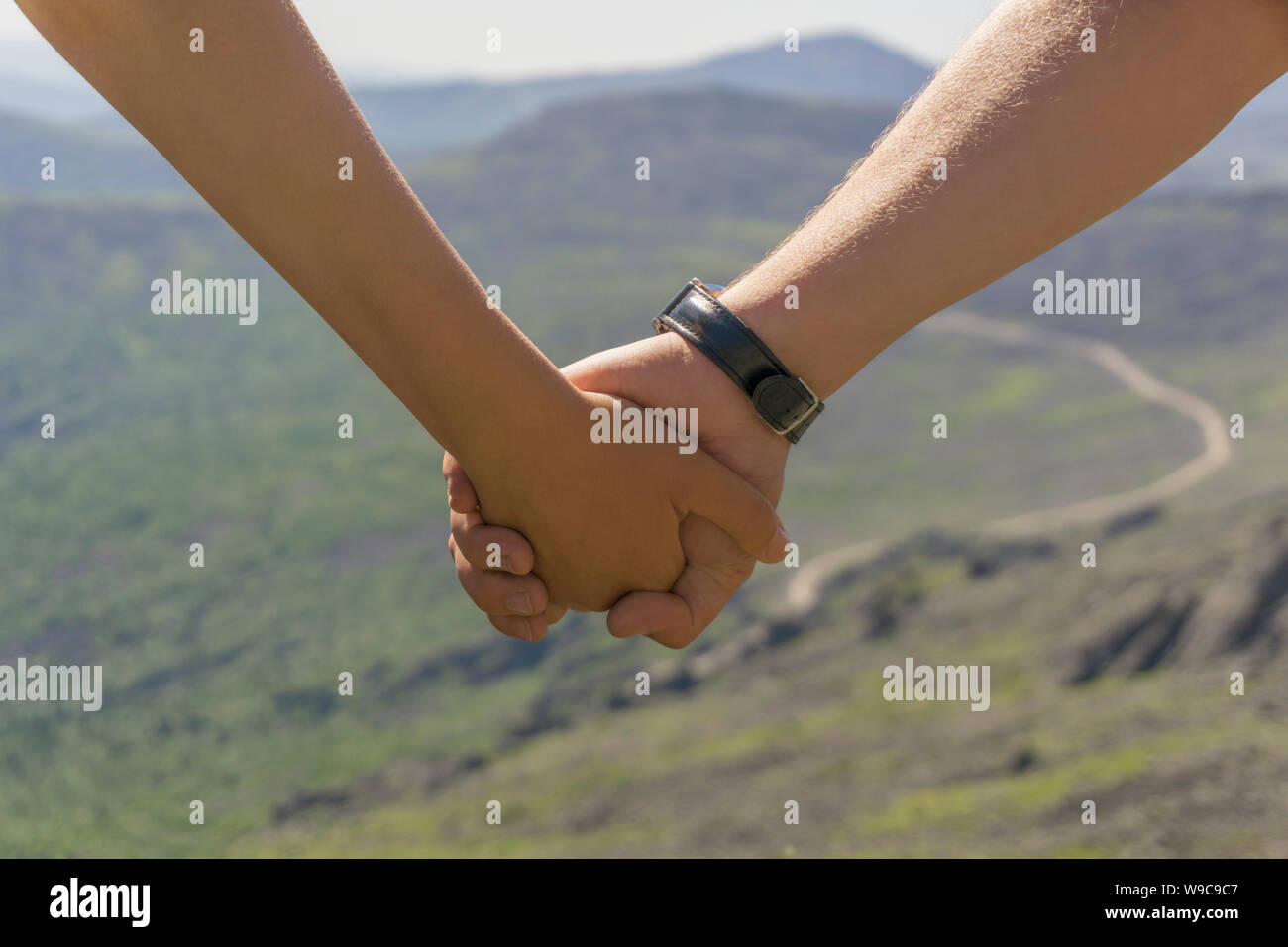 Reisende, Mann und Frau sind halten sich an den Händen (nur Hände sind in der Nähe gesehen) vor dem Hintergrund einer unscharfen Berggipfel in der Ferne Stockfoto