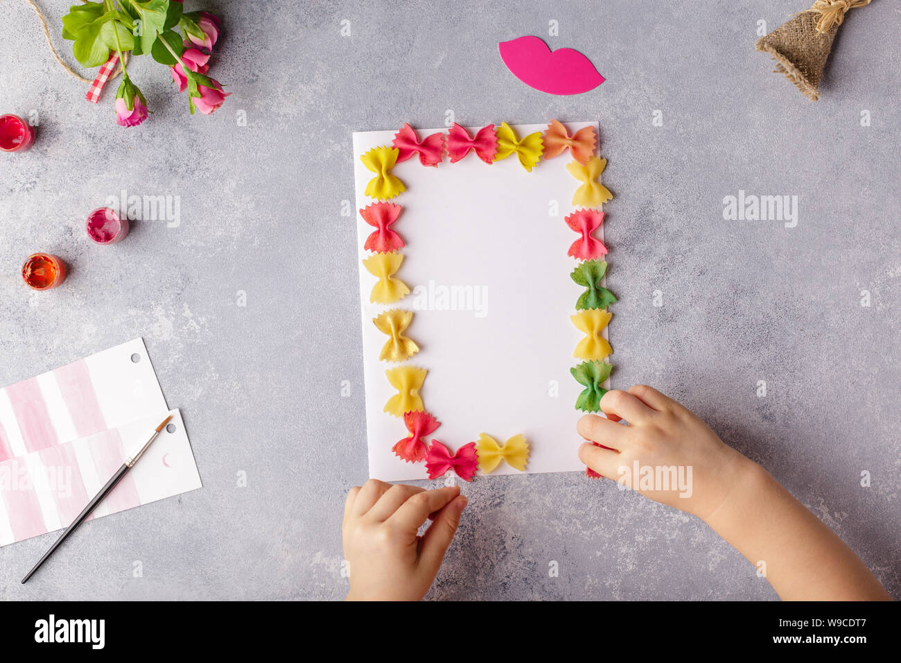 Papier basteln für Muttertag, 8. März oder Geburtstag. Kleines Kind tun einen Blumenstrauß aus farbigem Papier und bunte Nudeln. Stockfoto