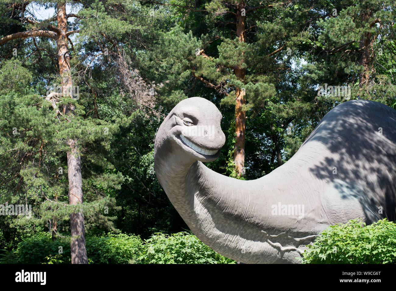 Grau cartoon gute Dinosaurier mit langem Hals kam aus dem nadelwald an einem Sommertag und lächelt, Skulptur Der brachiosaurus Stockfoto