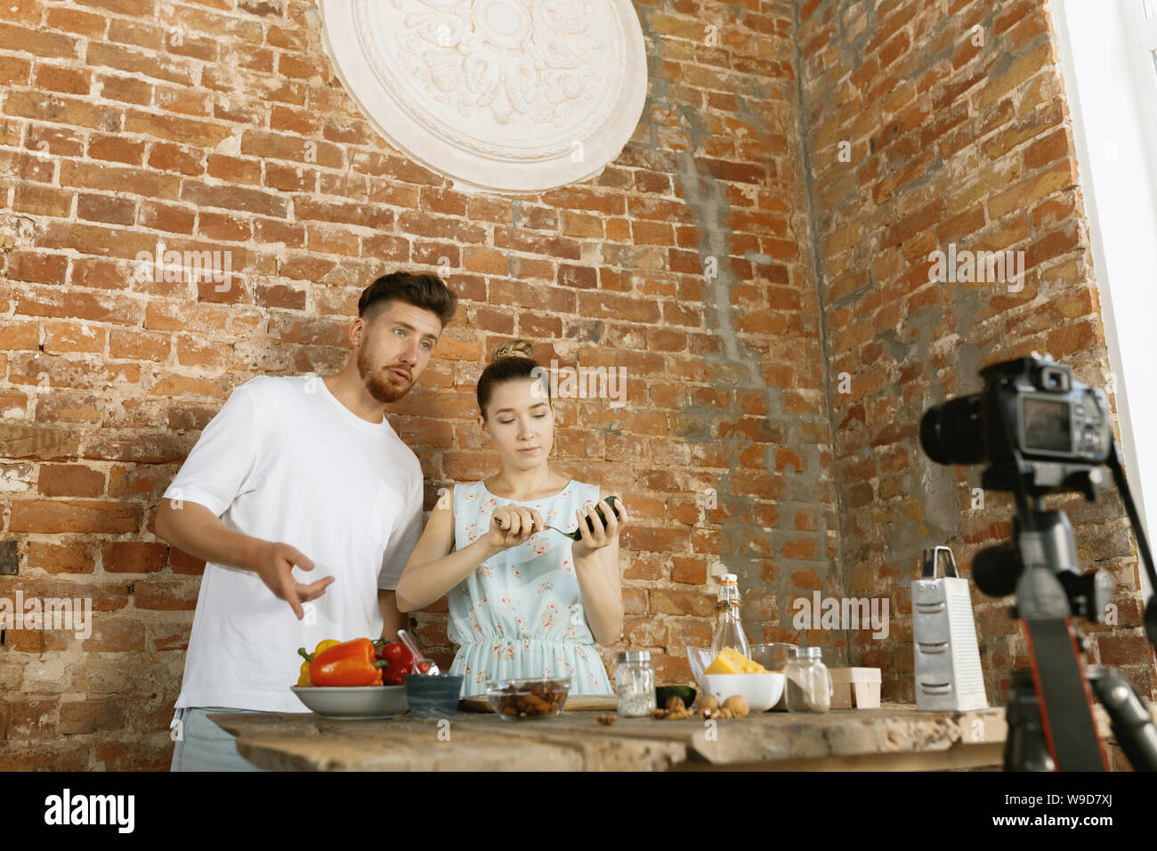 Vlogger und Blogger freier Job, essen Konzept. Junge kaukasier Paar zusammen kochen und Recording Live Video für Vlog und Social Media mit einer professionellen Kamera gegen die Mauer in ihrer Küche. Stockfoto