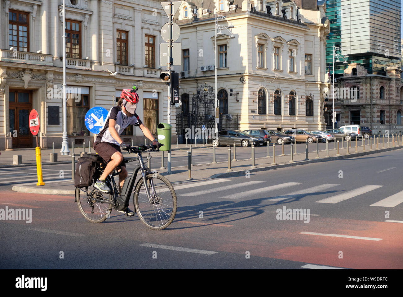 Radfahrer mit Helm, Kamera und oben, Verschmutzung Maske kreuzt Straße auf Radweg in der Innenstadt von Bukarest, Rumänien, Stockfoto