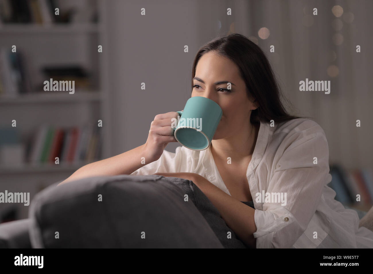 Frau trinkt Kaffee sitzen auf einer Couch in der Nacht zu Hause Stockfoto