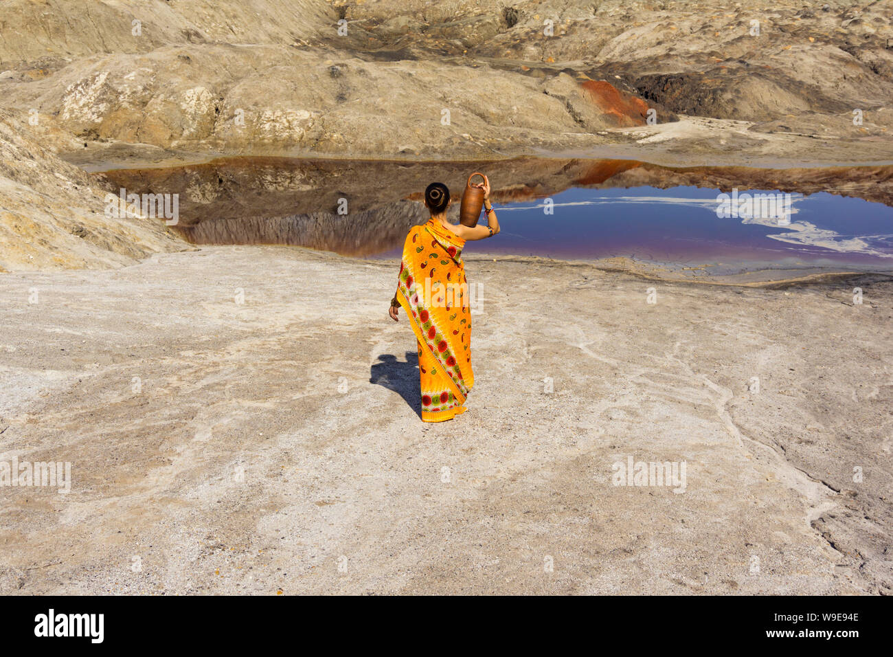 Ein Mädchen in einem Sari mit einem Krug auf ihrer Achsel geht für Wasser zu einem schmutzigen See in einer menschenleeren Landschaft Stockfoto